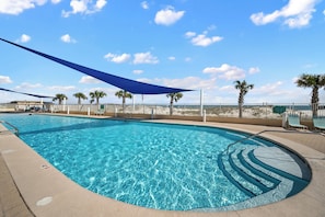 Una piscina azul cristalina con una zona de sombra, palmeras y una valla.