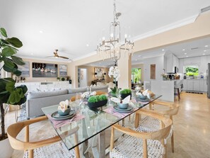 A modern dining area with a glass table, white wicker chairs, and a chandelier.