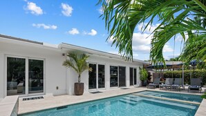 A modern pool area with clear blue water, a white building with large windows, and a palm tree. - Heated Pool Waterfront Retreat – A Fun, Sun-Soaked Florida Getaway on the Waterway Escape Now! (Fort Lauderdale)
