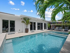 A modern pool area with clear blue water, a white building with large windows, and a palm tree. - Heated Pool Waterfront Retreat – A Fun, Sun-Soaked Florida Getaway on the Waterway Escape Now! (Fort Lauderdale)