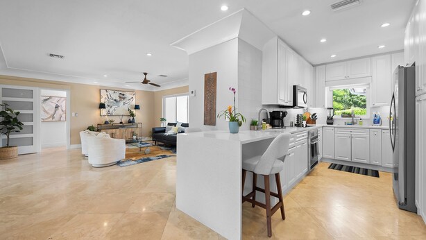 A modern kitchen with white cabinetry, a central island, and a dining area with a sofa and coffee table. - Heated Pool Waterfront Retreat – A Fun, Sun-Soaked Florida Getaway on the Waterway Escape Now! (Fort Lauderdale)