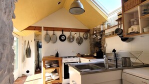 Una cocina con estufa a gas, pileta y varias ollas y sartenes colgadas en la pared.