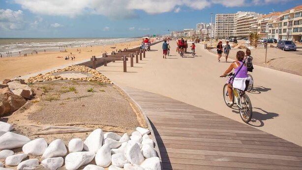 Une promenade de bord de mer avec une jetée en bois, une plage et des bâtiments en arrière-plan.