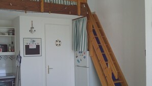 Une cuisine compacte avec une table en bois, un réfrigérateur et une échelle en bois adossée au mur.