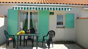 Une terrasse avec une table et des chaises, une porte verte et une petite fenêtre.