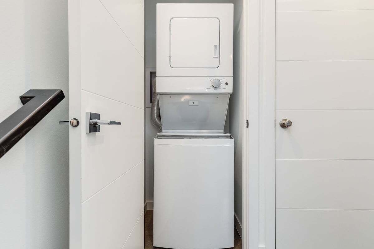 Een kleine, witte wasruimte met een ingebouwde wasmachine en droger, een klein bedieningspaneel en een deur met een handgreep.