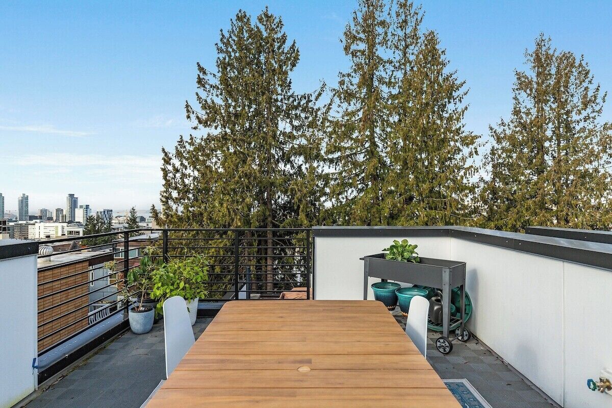 A rooftop terrace with a wooden table, potted plants, and a garden cart.