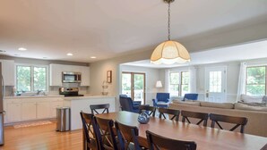 A modern kitchen with a dining area, a sofa, and a hanging light fixture. - 4 Mins to Bayside Beaches! (Eastham)