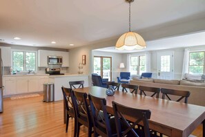 A modern kitchen with a dining area, a sofa, and a hanging light fixture. - 4 Mins to Bayside Beaches! (Eastham)