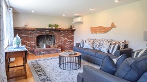 A living room with a brick fireplace, a sofa, a round coffee table, and a decorative wall piece. - 4 Mins to Bayside Beaches! (Eastham)