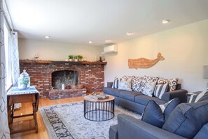 A living room with a brick fireplace, a sofa, a round coffee table, and a decorative wall piece. - 4 Mins to Bayside Beaches! (Eastham)