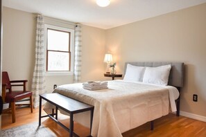 A bedroom with a bed, a bedside table, a chair, a lamp, and a window with curtains. - 4 Mins to Bayside Beaches! (Eastham)