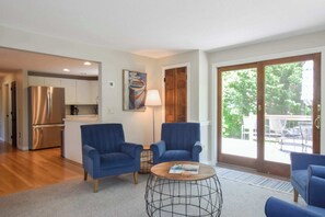A modern living room with two blue armchairs, a coffee table, and a kitchen in the background. - 4 Mins to Bayside Beaches! (Eastham)