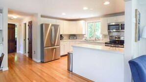 A modern kitchen with stainless steel appliances, a central island, and white cabinetry. - 4 Mins to Bayside Beaches! (Eastham)