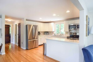 A modern kitchen with stainless steel appliances, a central island, and white cabinetry. - 4 Mins to Bayside Beaches! (Eastham)