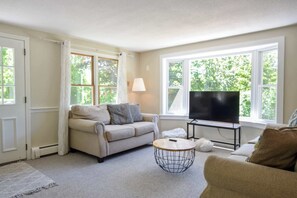 A living room with a sofa, a coffee table, a TV, and a window with curtains. - 4 Mins to Bayside Beaches! (Eastham)