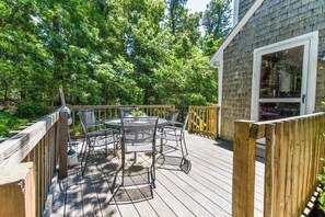 A wooden deck with a table and chairs, surrounded by trees. - Minutes to Oceanside Beaches! (Eastham)