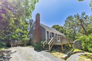 A rustic house with a chimney, wooden deck, and a gravel driveway.