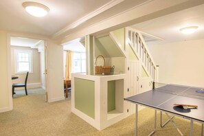 A room with a ping pong table, a chair, a small table with a basket, and a staircase. - Minutes to Oceanside Beaches! (Eastham)