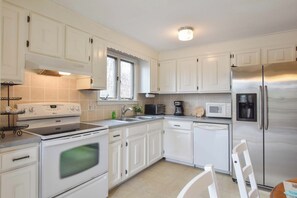 A modern kitchen with white cabinets, stainless steel appliances, and a window providing natural light.