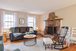 A living room with a fireplace, a sofa, a rocking chair, and a small table with a lamp.