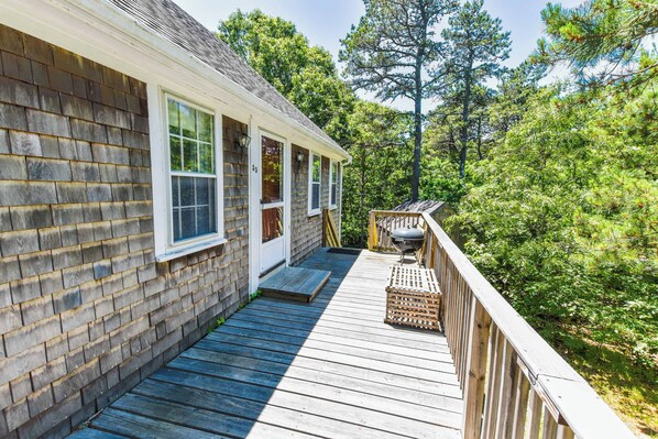 A wooden deck with a barbecue grill, a covered porch, and a view of a forested area. - Minutes to Oceanside Beaches! (Eastham)