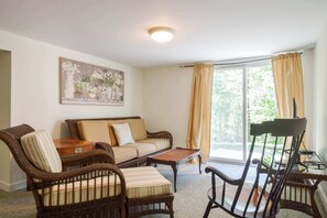 A living room with wicker furniture, a sofa, a coffee table, and a painting on the wall. - Minutes to Oceanside Beaches! (Eastham)