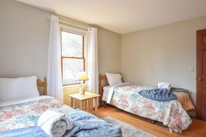 A bedroom with two beds, a window with curtains, a bedside table with a lamp, and a door. - Minutes to Oceanside Beaches! (Eastham)