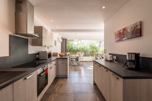 A modern kitchen with a central island, built-in oven, and a dining area with a view of greenery.