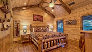 Un dormitorio rústico de madera con cama, dos mesitas de noche, ventilador de techo y decoración en la pared.