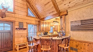 Interior rústico de una cabaña de madera con una zona de bar, sillas de madera y una decoración de cabeza de venado.