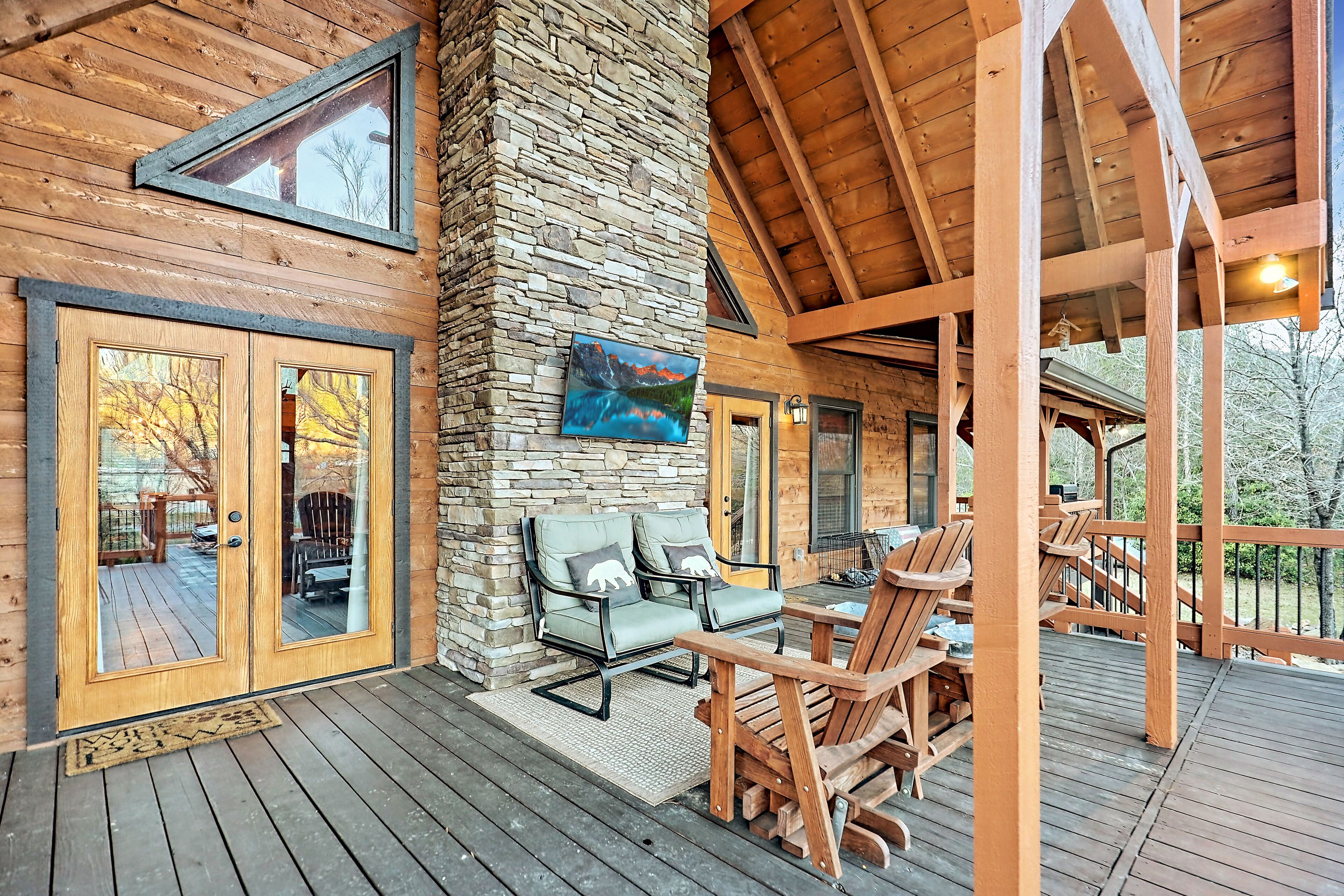 A wooden deck with outdoor seating, stone walls, and a large window.