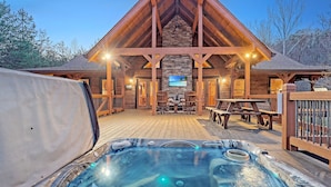 Una cabaña de madera con jacuzzi, mobiliario exterior y chimenea de piedra.