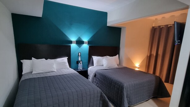 Habitación de hotel con dos camas, una mesita de noche con lámpara, y un baño visible a través de una puerta abierta.