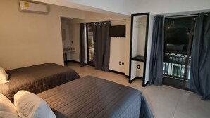 Habitación de hotel con dos camas, televisión, balcón con cortinas y puerta corrediza.