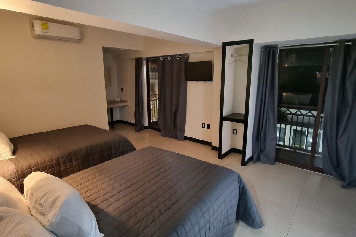 A hotel room with two beds, a TV, a balcony with curtains, and a sliding door.