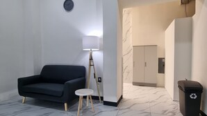 Una sala de estar moderna con un sofá negro, una mesita redonda pequeña, una lámpara de pie y un cubo de basura.