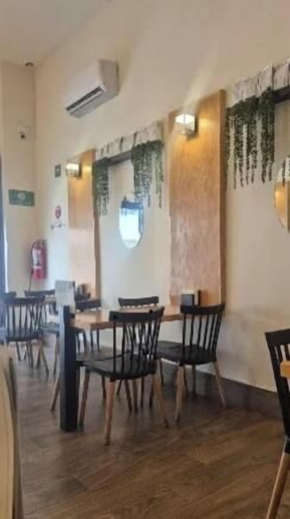 Un interior de restaurante con suelo de madera, sillas negras y plantas colgantes.