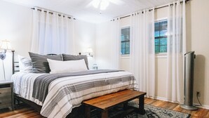 A bedroom with a bed, bedside tables, a bench, a TV, and a window with blinds. - Luxurious cabin with fire pit, kayaks, and dock. (Arley)