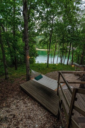 Eine Hängematte auf einer Holzterrasse mit Blick auf einen See, umgeben von Bäumen.