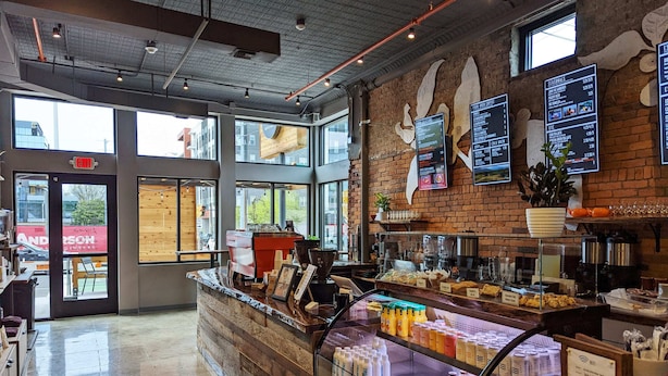A coffee shop interior with a counter displaying various beverages, a menu board, and a brick wall. - Songwriter's Suite: Luxe Music Row Stay! (Nashville)
