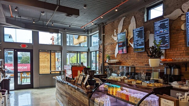 A coffee shop interior with a counter displaying various beverages, a menu board, and a brick wall. - Songwriter's Suite: Luxe Music Row Stay! (Nashville)