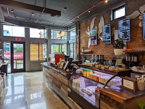 Enjoy a warm atmosphere in this cozy coffee shop with a wooden counter, glass display case, and brick wall.