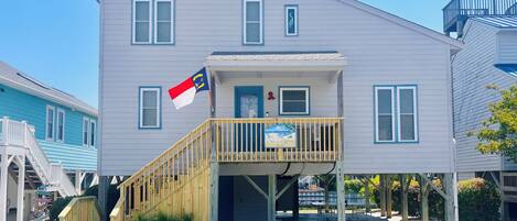 A two-story building with a wooden deck, a flag, and a sign that reads 'Out of Office.'