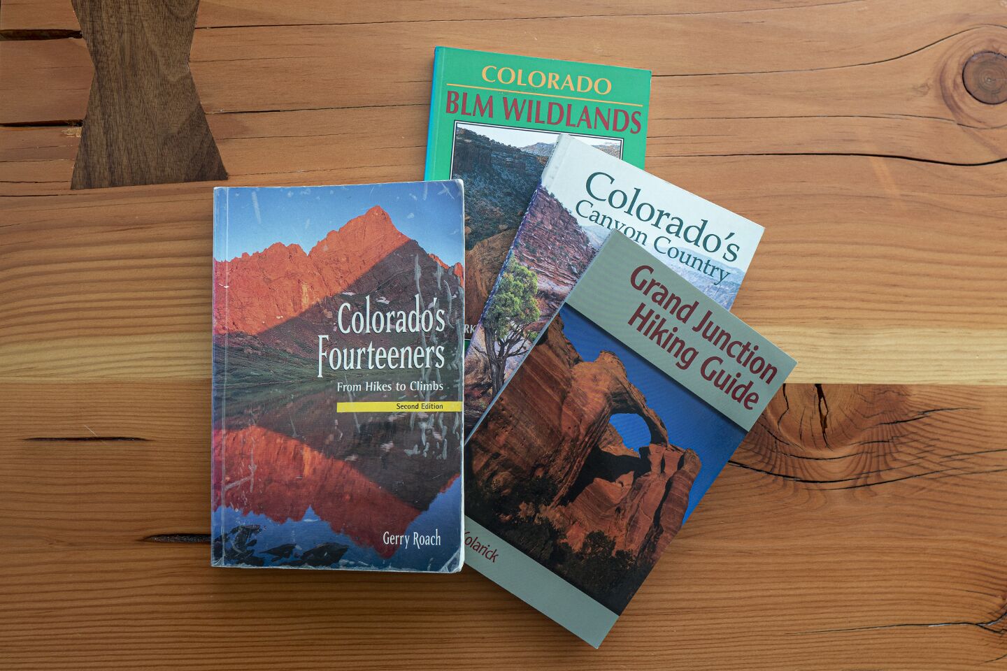 Drie boeken met de titels 'Colorado's Fourteeners', 'Colorado's Canyon Country' en 'Grand Junction Hiking Guide' op een houten oppervlak.