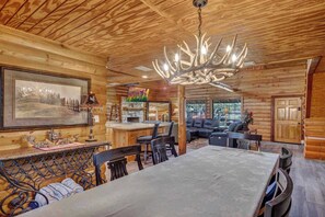 A log cabin interior with a dining area, fireplace, and a chandelier.