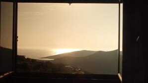 Une pièce dotée d’une grande fenêtre donnant sur l’océan et les collines au coucher du soleil.