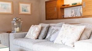 A living room with a sofa, decorative pillows, a wall-mounted shelf with items, and framed pictures. - Chalet Alpen, 5 bedrooms, sauna, near Megève and the ski slopes. (Praz-sur-Arly)