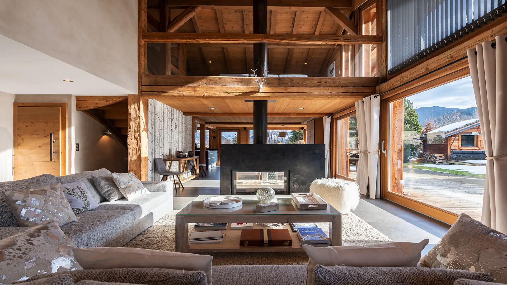 A spacious living room with a fireplace, large windows, and a high ceiling.