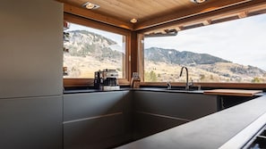 A modern kitchen with a built-in sink, a coffee machine, and a view of a mountainous landscape. - Chalet Alpen, 5 bedrooms, sauna, near Megève and the ski slopes. (Praz-sur-Arly)